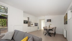 A modern kitchen with white cabinets, a dining area with a table and chairs, and a gray sofa with a yellow pillow. - Modern Lodge With Infrared Sauna, Near Helmond (Mierlo)