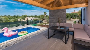 Un espacio al aire libre techado con piscina, una mesa y un sofá.