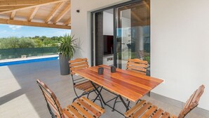 Un patio techado con una mesa y sillas de madera, una planta en maceta y vistas a la piscina y la vegetación.