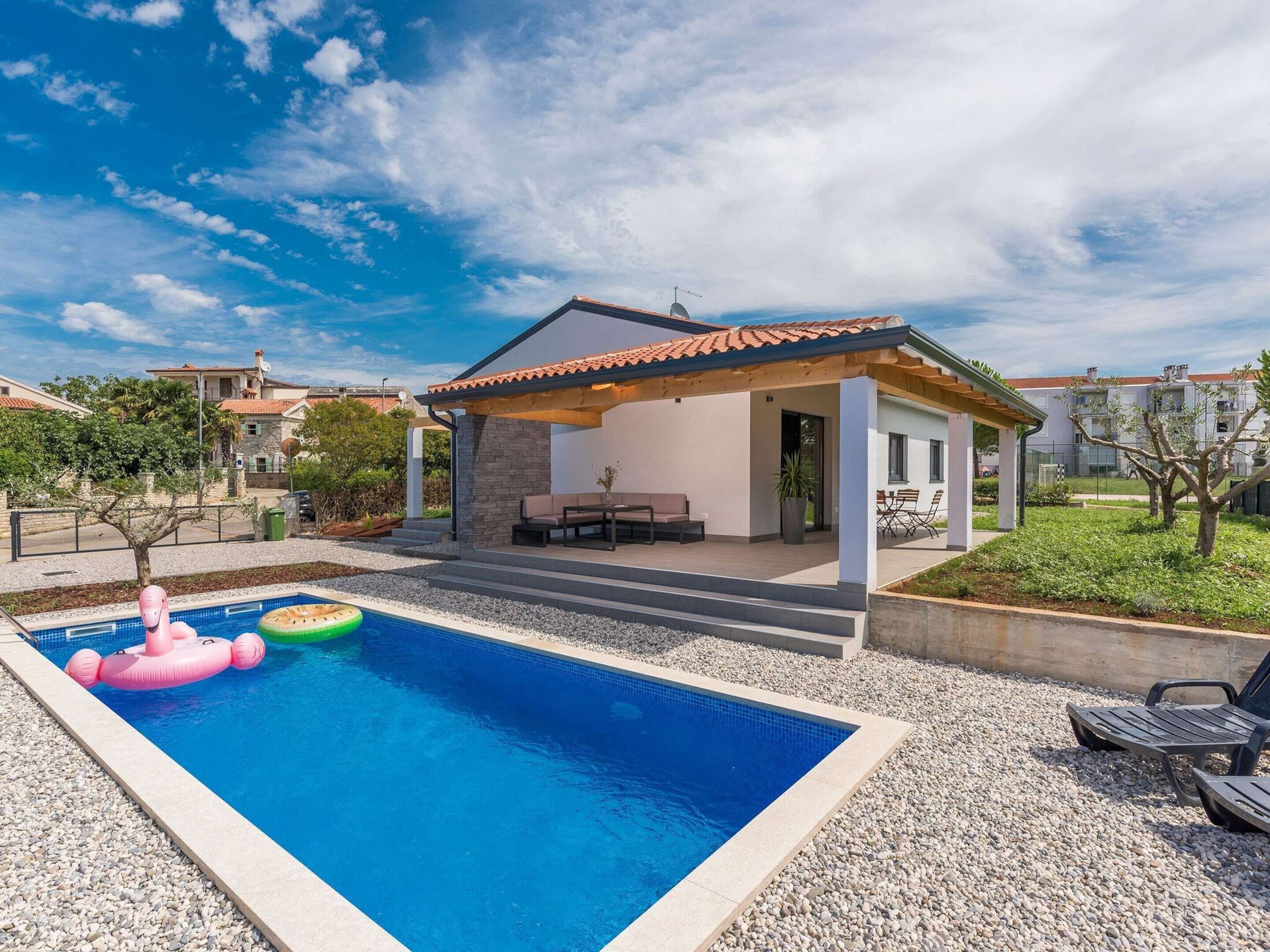 Ein modernes Haus mit Schwimmbad, Sitzgelegenheit im Freien und einem Garten.