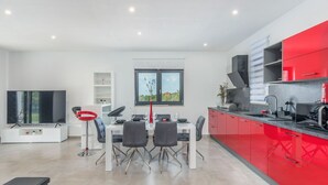 Una cocina moderna con armarios rojos, un comedor con mesa y sillas blancas, y un televisor de pantalla plana grande.