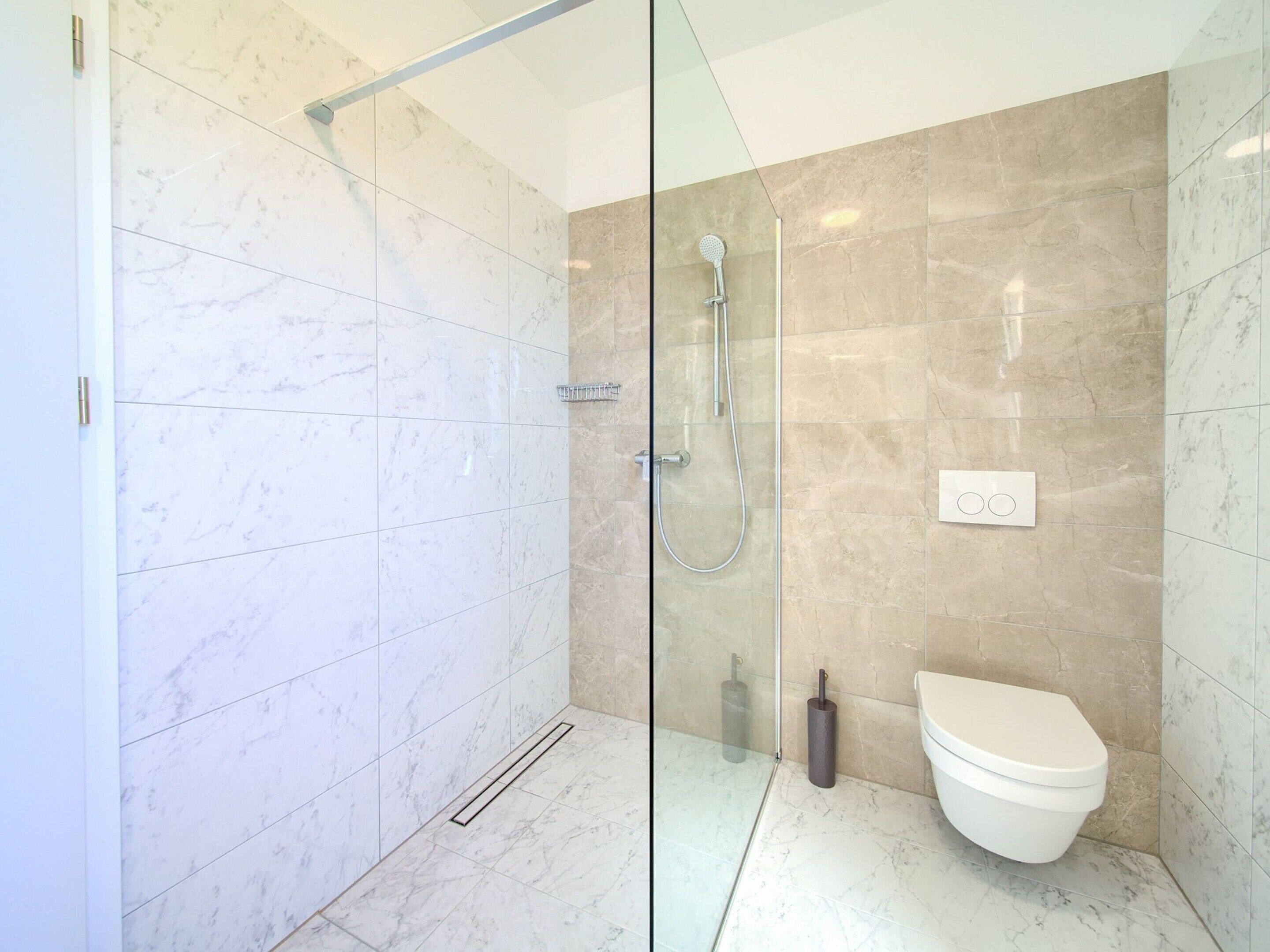 A modern bathroom with a glass shower enclosure, a toilet, and a hand dryer.