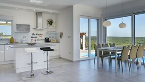 A modern kitchen with a central island, bar stools, and a dining area with a table and chairs. - Villa in Peroj With Pool Near Barbariga Beach (Vodnjan)
