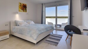 A modern bedroom with a large bed, a desk, and a chair, a painting on the wall, and a balcony with a view. - Villa in Peroj With Pool Near Barbariga Beach (Vodnjan)