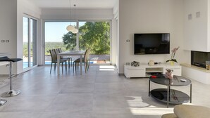 A modern living room with a dining area, a flat-screen TV, and a fireplace. - Villa in Peroj With Pool Near Barbariga Beach (Vodnjan)