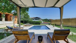 Un espace aménagé au bord de la piscine, avec deux chaises longues, une petite table et une vue sur une maison en arrière-plan.