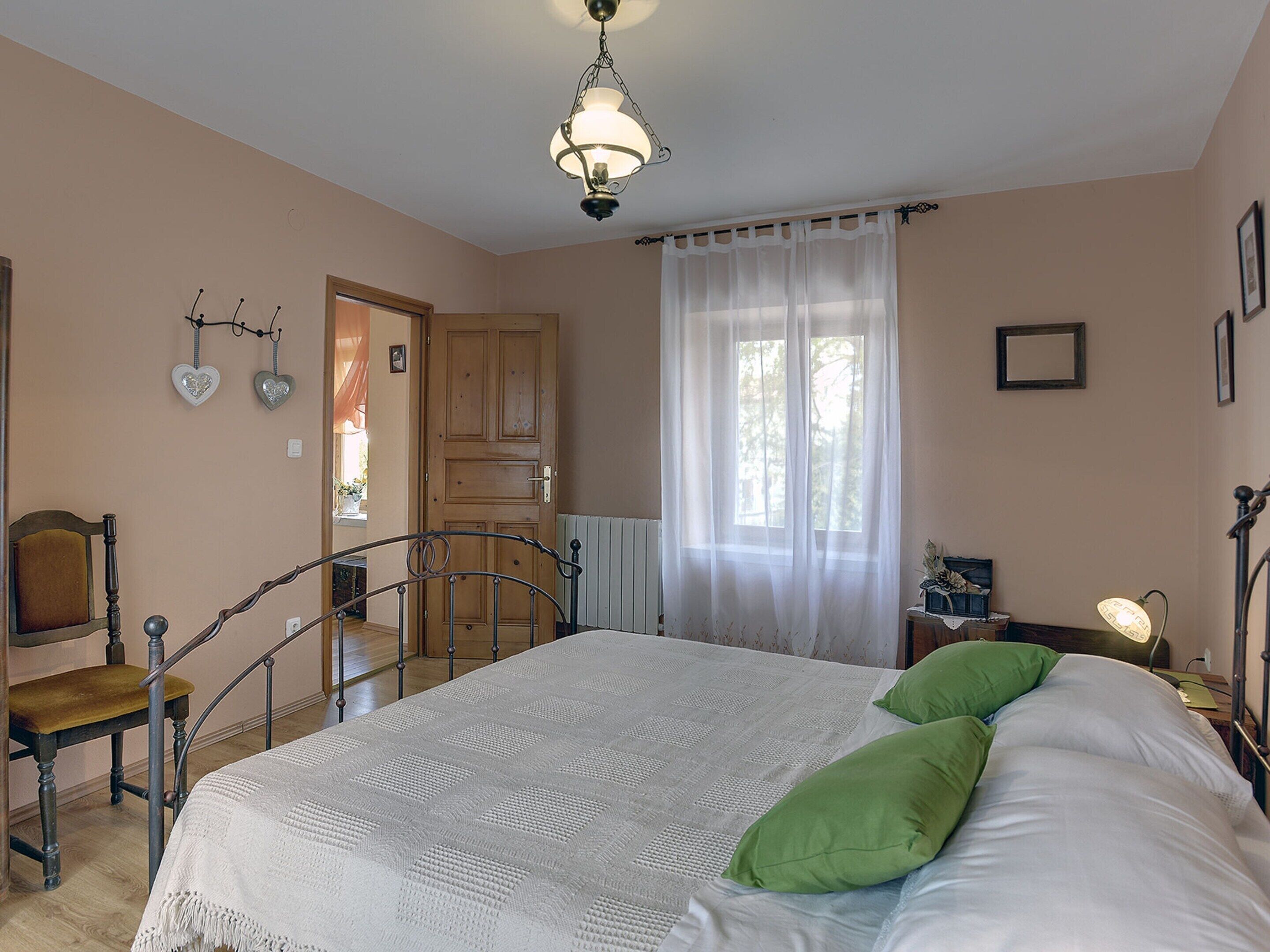 A bedroom with a bed, a chair, a wooden door, and a window with curtains.