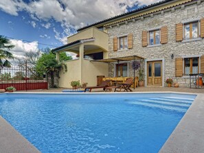 Et toetagers stenhus med swimmingpool, udendørs møbler og en overdækket terrasse.