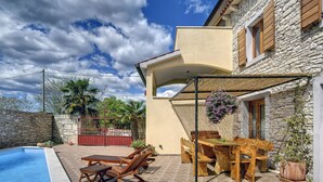 Un espace aménagé au bord de la piscine, avec une table et des chaises, une pergola et un mur en pierre.