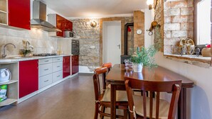 A modern kitchen with red cabinets, a stone wall, and a dining area with wooden chairs. - Villa in Istria With Pool Near Croatian Sea (Svetvincenat)
