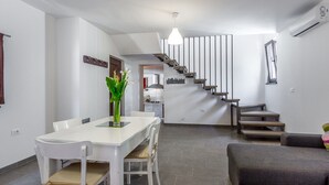 A modern kitchen with white cabinetry, a dining table with chairs, a staircase with wooden steps, and a grey sofa in the living area. - Villa in Istria With Pool Near Croatian Sea (Svetvincenat)