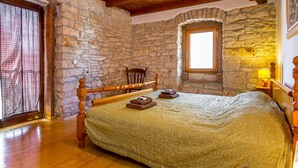 A cozy bedroom with a stone wall, wooden ceiling beams, a bed with a green bedspread, a chair, and a window with a view. - Villa in Istria With Pool Near Croatian Sea (Svetvincenat)