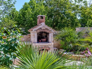 Cocina exterior de piedra con chimenea, rodeada de abundante vegetación y un muro de piedra.