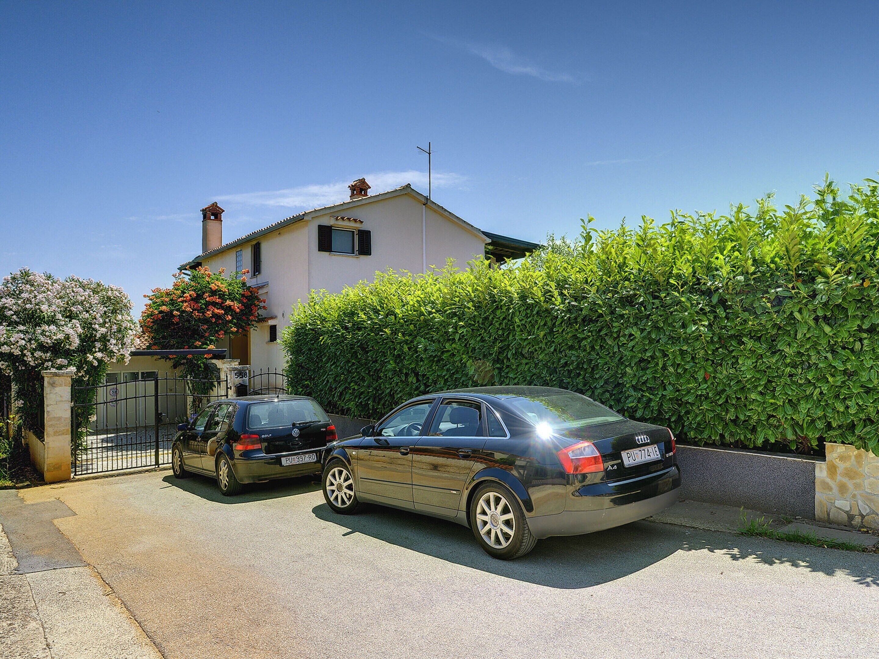 A two-story house with a garage, parked cars, and a well-maintained hedge.