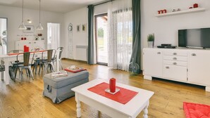 Ein modernes Wohnzimmer mit Essbereich, einem weißen Sofa, einem roten Tisch und einem Fernseher auf einem weißen Schrank.