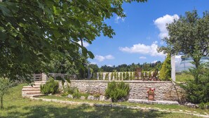 A stone wall garden with a seating area, surrounded by greenery and a clear blue sky. - Spacious Holiday Home in Svetvincenat With Pool (Svetvincenat)