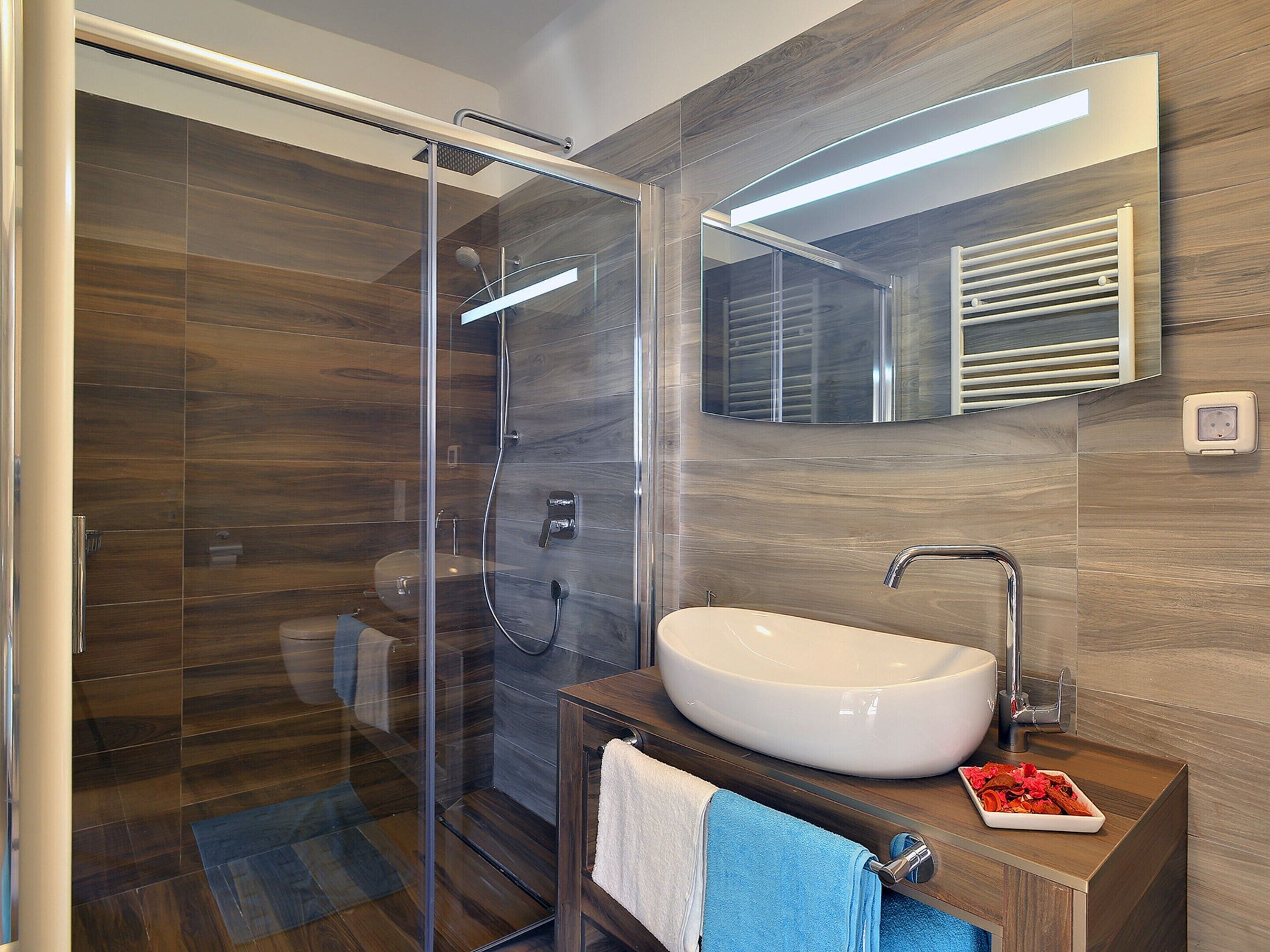 A modern bathroom with a glass shower enclosure, a white sink, and a wooden vanity.
