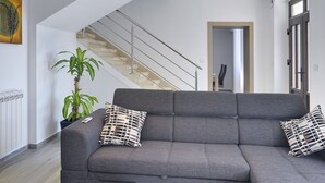 A modern living room with a grey sofa, two patterned cushions, a potted plant, and a staircase leading to another room. - Holiday Home in Liznjan Near the Beach (Liznjan)