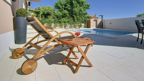 A poolside area with lounge chairs and a table, a small pool, and a view of trees and a building in the background. - Holiday Home in Liznjan Near the Beach (Liznjan)