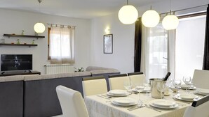 Ein moderner Essbereich mit einem langen Tisch, gedeckt für vier Personen, einer Couch und einem Fernseher im Hintergrund.