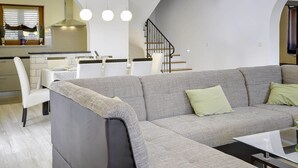 Ein modernes Wohnzimmer mit grauem Sofa, einem Esstisch und einer Küchenzeile im Hintergrund.