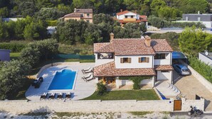 Eine Villa mit Swimmingpool, einer überdachten Terrasse und Blick auf den umliegenden Wald.