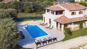 Ein zweistöckiges Haus mit Swimmingpool, Sitzgelegenheit im Freien und Blick auf die umliegende Grünfläche.