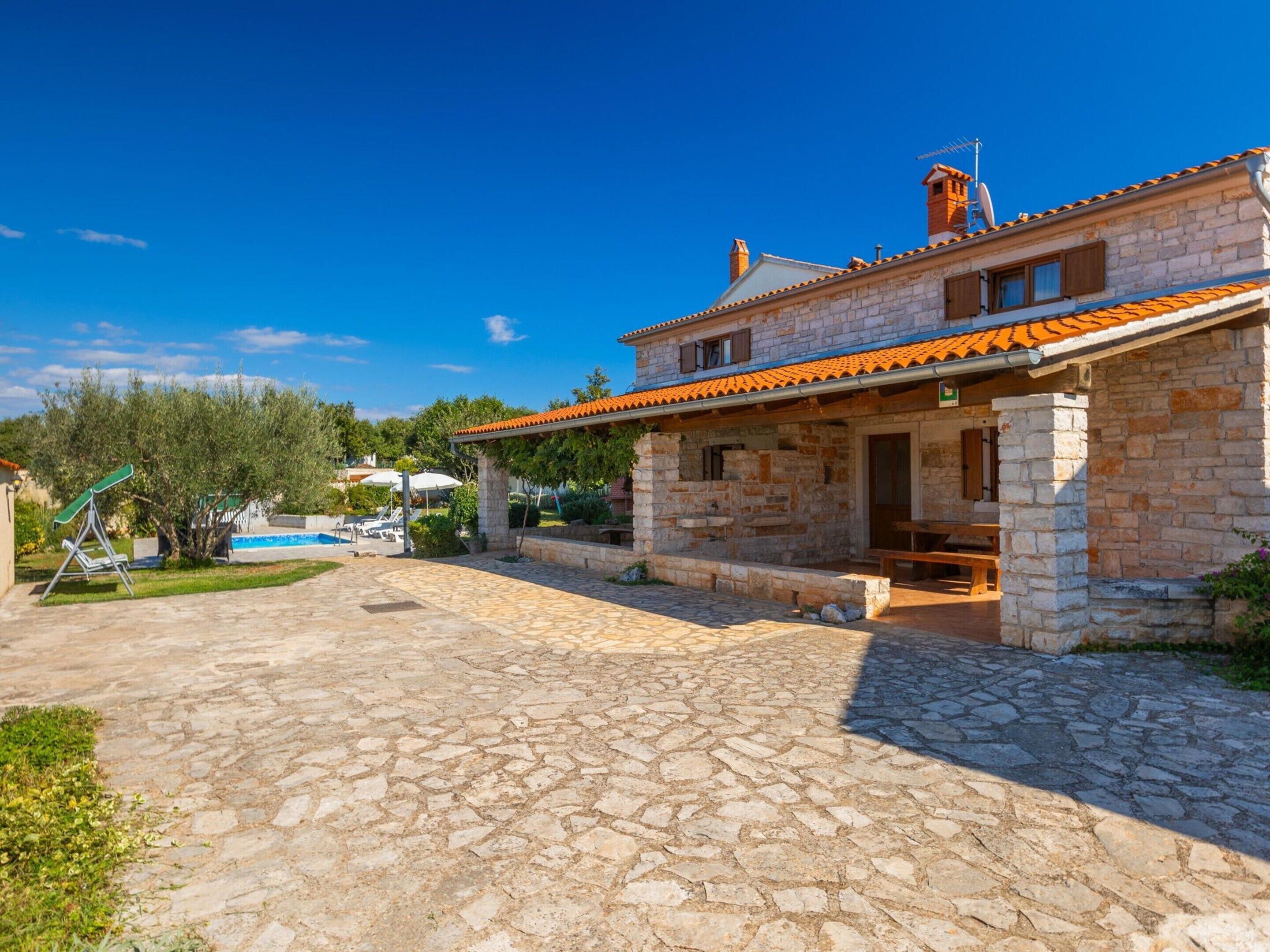 A stone house with a tiled roof, a swimming pool, and a stone patio.