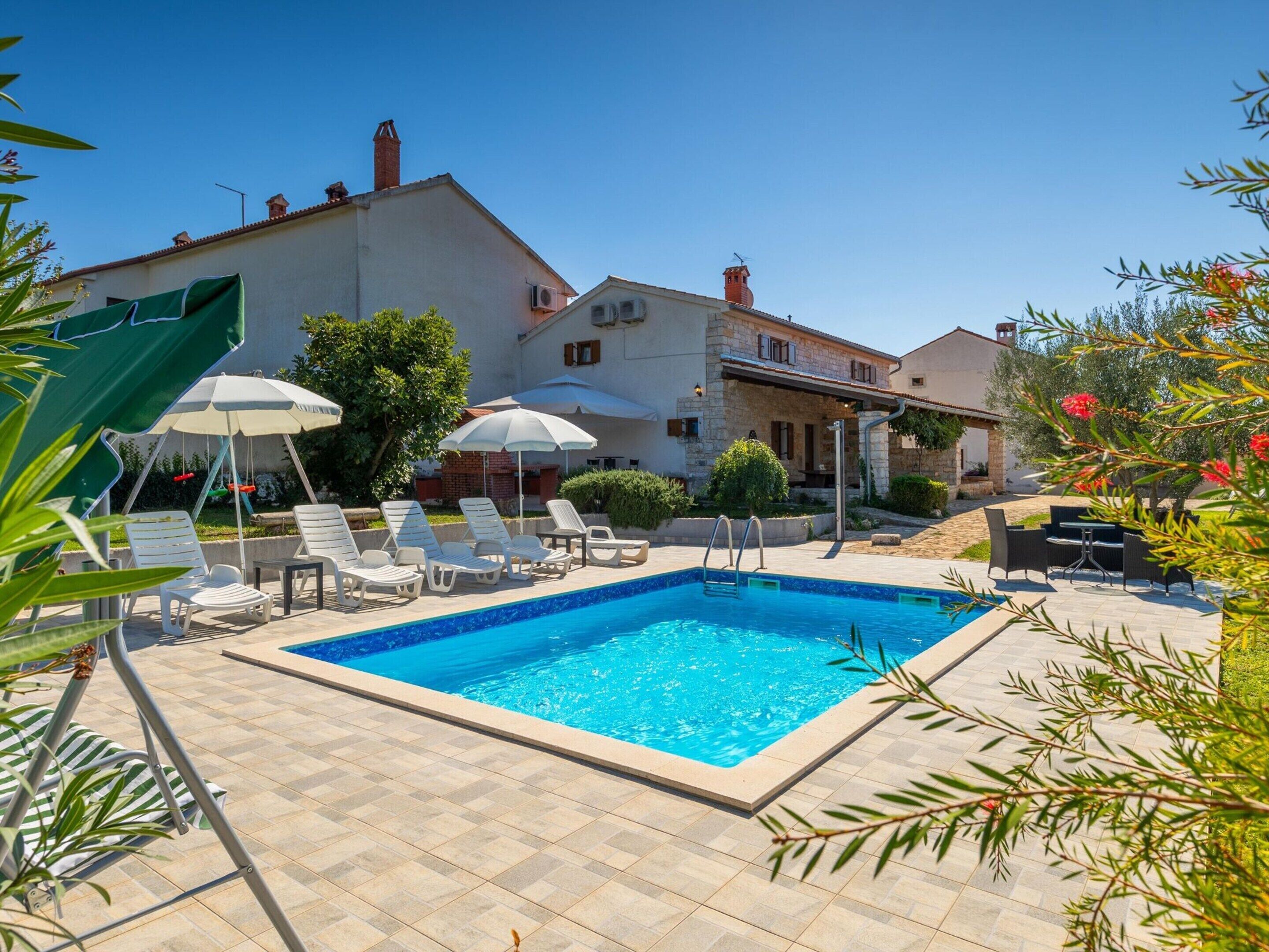 A swimming pool with lounge chairs and umbrellas, surrounded by stone buildings and greenery.