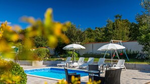 A poolside area with lounge chairs and umbrellas, surrounded by greenery. - Holiday Home in Segotici With Private Pool (Marcana)