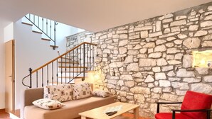 A living room with a stone wall, a wooden staircase, a sofa with patterned cushions, a red chair, and a wooden coffee table. - Holiday Home in Segotici With Private Pool (Marcana)