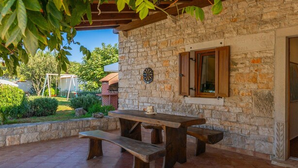 A stone patio with a wooden table and benches, a dartboard, and a window with shutters. - Holiday Home in Segotici With Private Pool (Marcana)