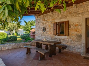 A stone patio with a wooden table and benches, a dartboard, and a window with shutters. - Holiday Home in Segotici With Private Pool (Marcana)