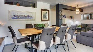 Un espace repas moderne avec une table en bois et six chaises, un canapé et un lustre.