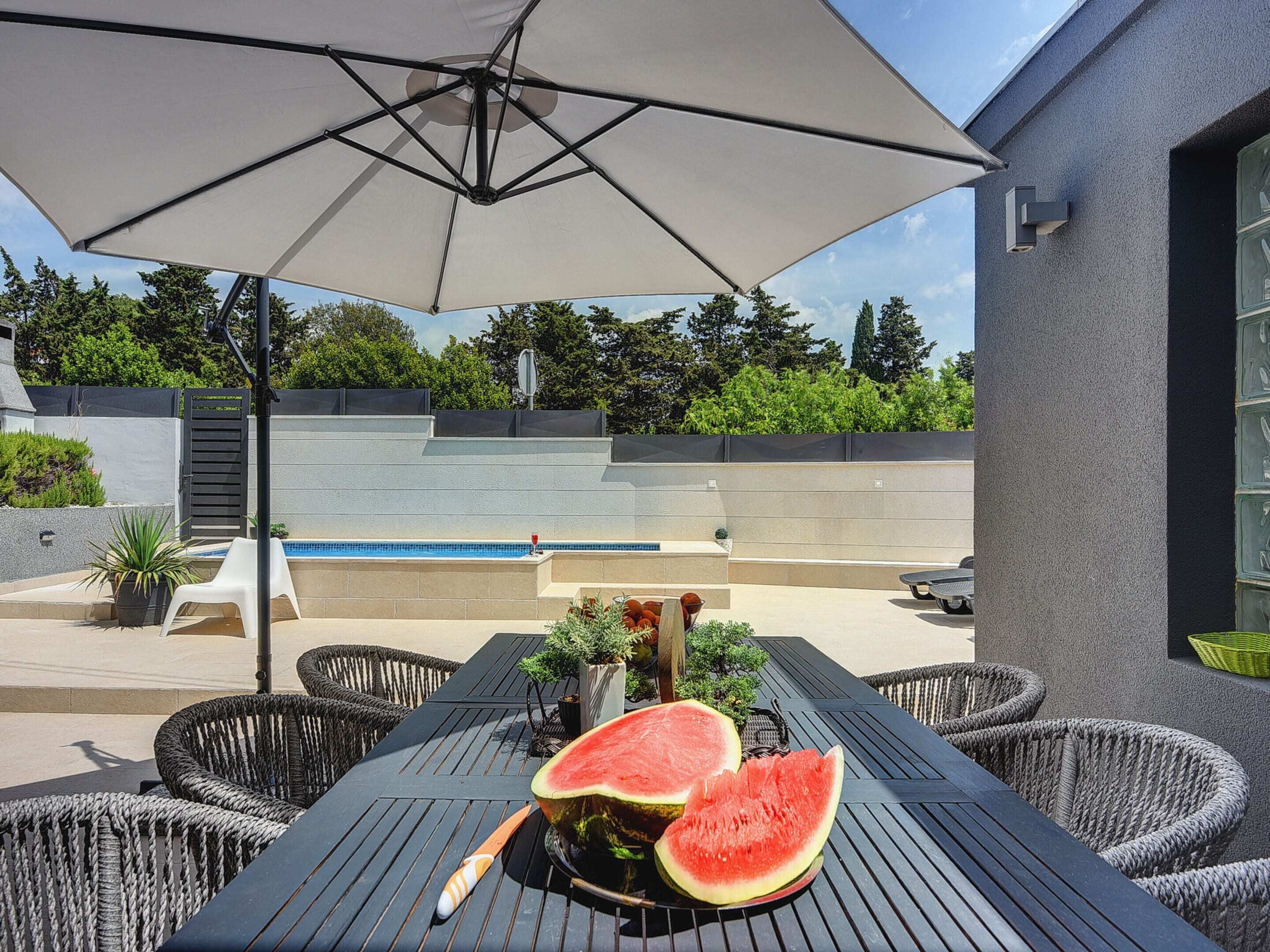 A patio with a pool, outdoor furniture, and a watermelon on a table.