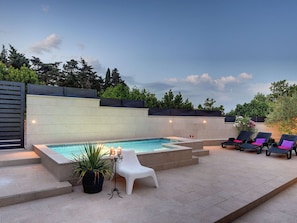 Uma área de piscina com hidromassagem, espreguiçadeiras e um vaso de planta.