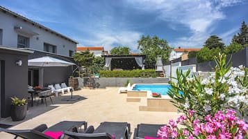 A backyard with a swimming pool, lounge chairs, and a barbecue area.