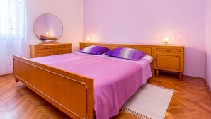 A bedroom with a wooden bed, two bedside tables, a round mirror, and a window with sheer curtains. - Apartment in Medulin Near the Sea (Medulin)