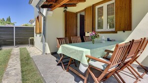 Patio esterno con tavolo imbandito per quattro persone, sedie di legno e un pergolato in legno.