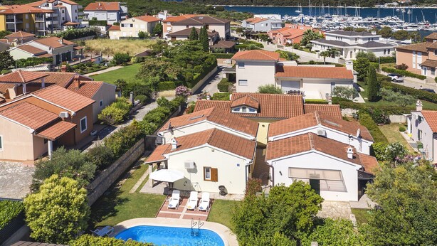 Una zona residenziale costiera con case, una piscina e un porto turistico sullo sfondo.