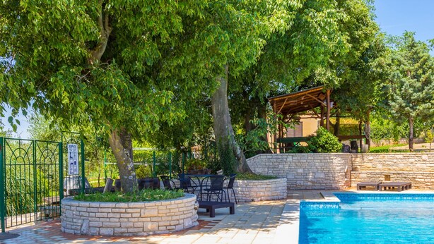 Une piscine bordée de pierres, entourée d’espaces de détente en plein air et d’arbres.