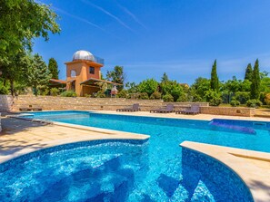 A swimming pool with lounge chairs, a stone wall, and a building with a dome in the background. - Peaceful Apartment in Pula With Swimming Pool (Liznjan)
