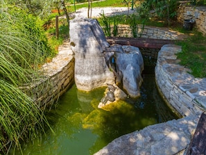 Une structure en pierre agrémentée d’un élément aquatique, entourée de verdure.