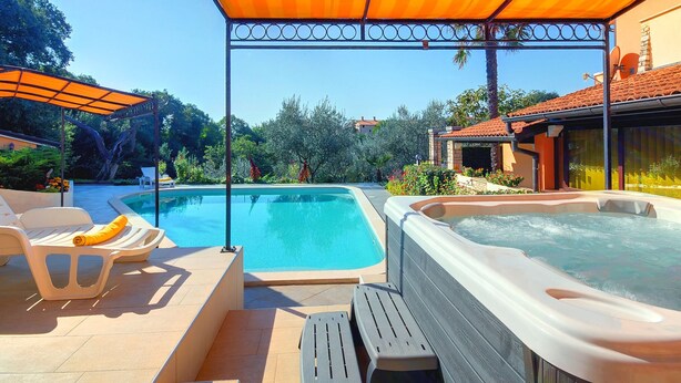 Een zwembad met een jacuzzi, ligbedden en een overdekt terras.