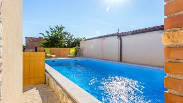Swimmers can enjoy the pool surrounded by a low wall and a fence.