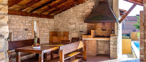 An outdoor kitchen with stone walls, wooden furniture, and a brick oven.
