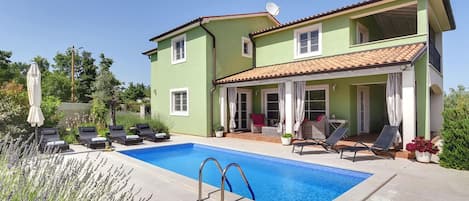 A two-story house with a swimming pool, outdoor seating, and a garden.
