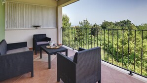 Un balcón con mobiliario de mimbre, una mesa con tetera y vistas a la vegetación.