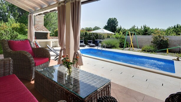Un espacio al aire libre cubierto con piscina, muebles de mimbre y una mesa de cristal.
