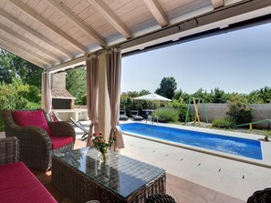 A covered outdoor area with a pool, wicker furniture, and a glass table. - Detached Villa With Swimming Pool in the East of Istria Near the Sea (Marcana)